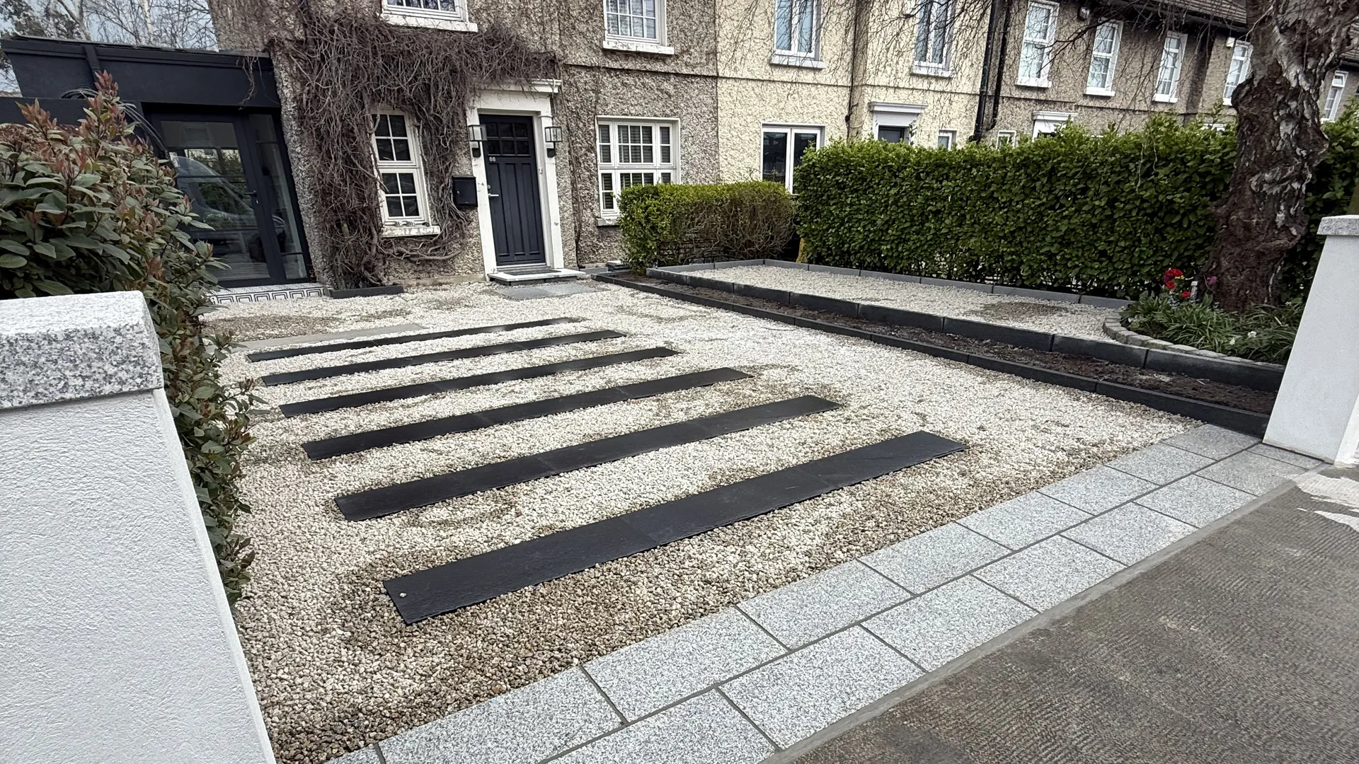 Finished gravel driveway with dark paving strips and a granite entrance apron.